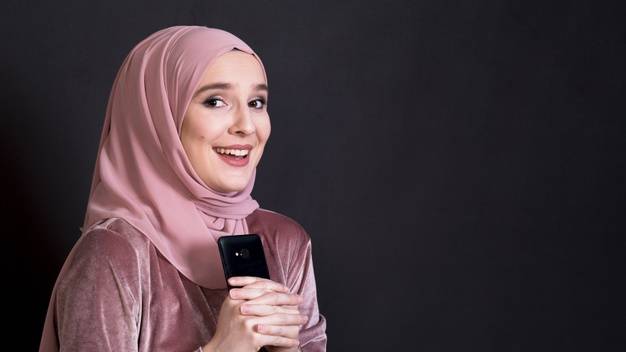 beautiful-muslim-woman-looking-camera-holding-mobile-phone-black-background